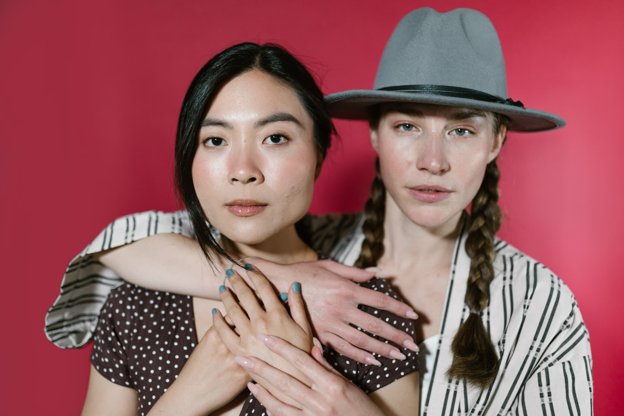 Two women standing closely together against a vivid red background